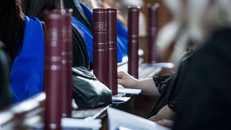 A row of graduation scrolls stand vertically in front of each graduate seated in pews