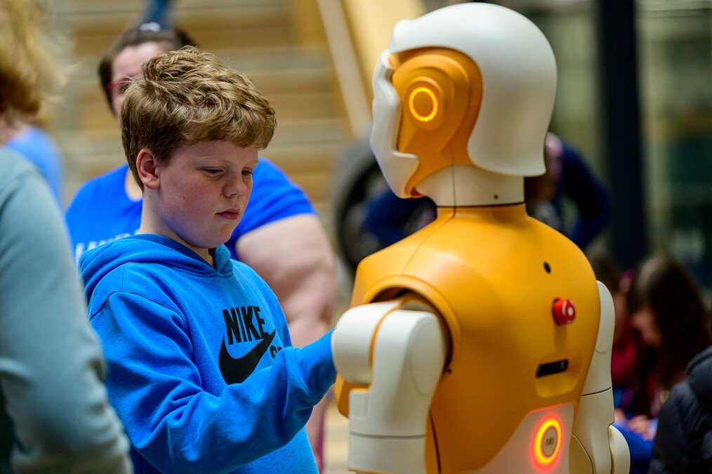 A young man with reddish hair plays with an ARI humanoid robot