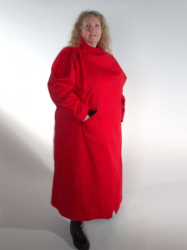 A woman stands wearing a long red coat and black boots.