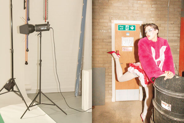 Man in a short skirt, furry pink jumper, white tights and red high heels kicks their right foot up behind them in a photo studio