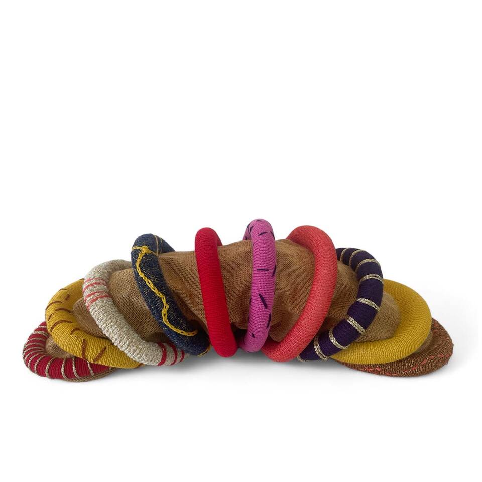 Colorful woolen bracelets stacked neatly on a white surface.