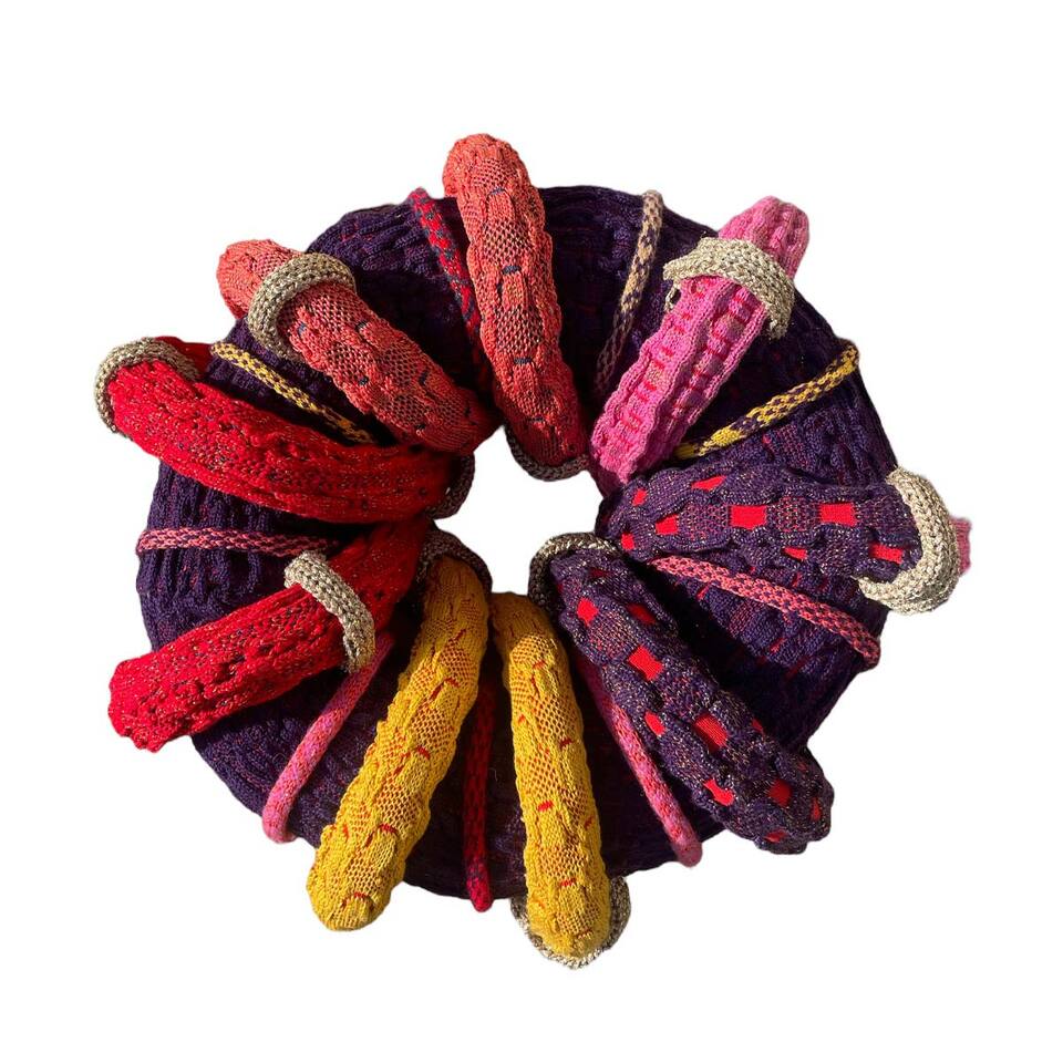 A vibrant wreath hand crafted from yarn, adorned with an assortment of colorful bands and ropes.