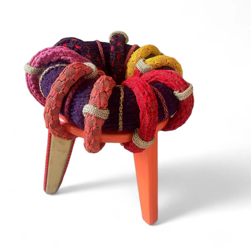A stool with vibrant knitted fabric cushion, adding a pop of color and texture to the furniture piece.