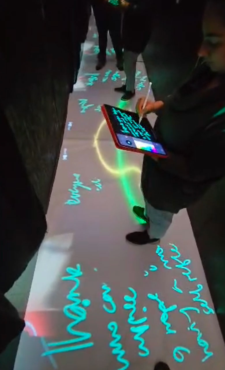 Person writing on a tablet computer as the text is projected onto the floor in front of them