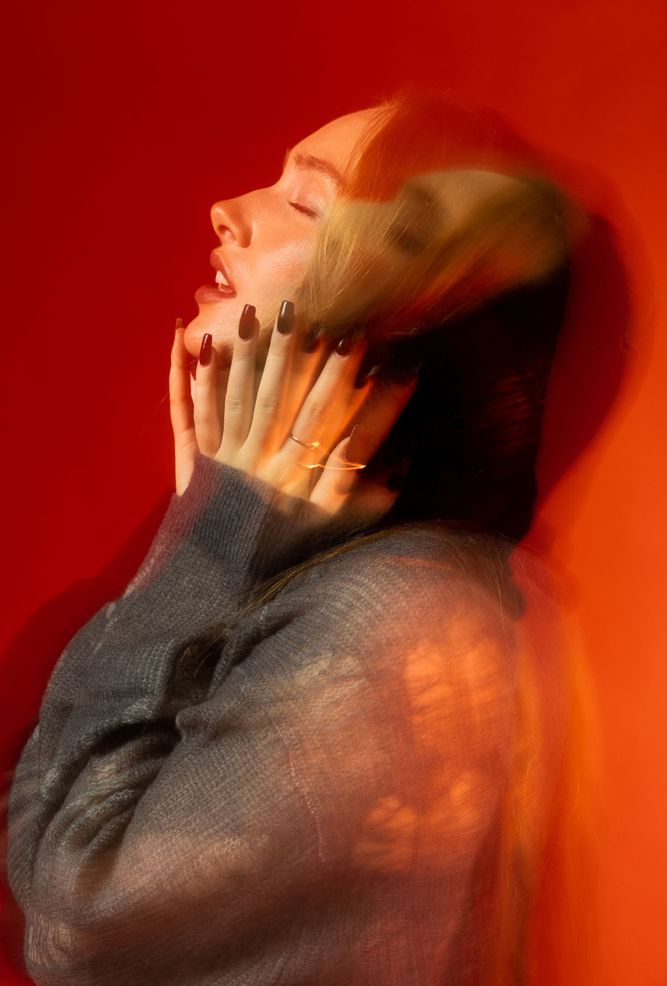 A double exposure of a young woman with eyes closed and lips parted with hands to her face