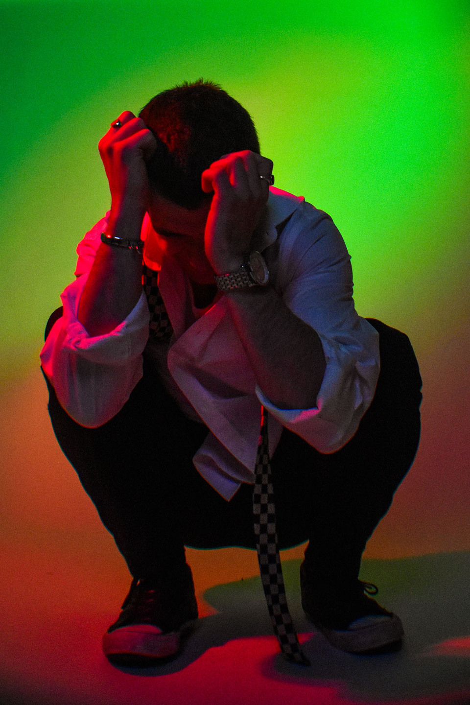 Young person crouched with hands in front of their head bathed in a green and orange light