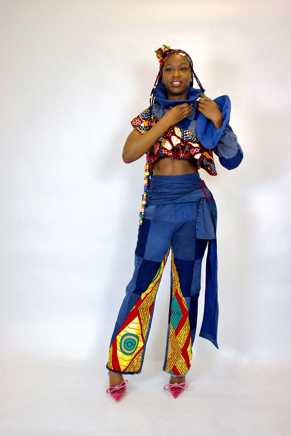 Woman models an African print single sleeved top and trousers in blue, red, orange and teal with upcycled denim sections, waistband and single flared sleeve.