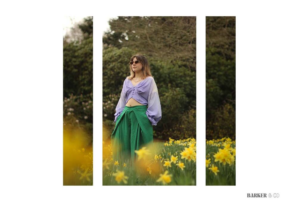 Woman in purple top and green skirt standing in a field of daffodils.