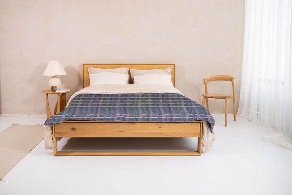  Image of a bed featuring a blue plaid blanket and wooden frame.