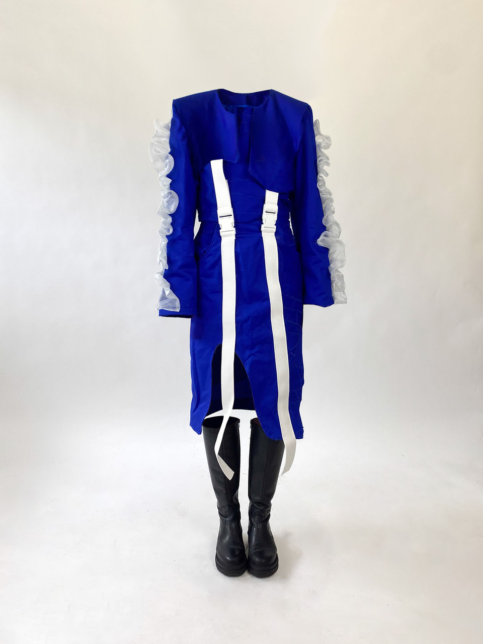 Blue collarless skirt suit with full length vertical white braces in front, crimped white lace details on the outer sleeves and knee length black flat soled boots by Gosia Czerwinska