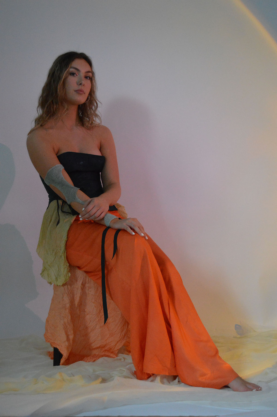 Barefoot, seated female model wearing black bodice and orange skirt designs inspired by Botticelli's 'The Birth of Venus'