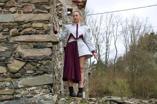 Woman models a Karen Heath design skirt and jacket beside the wall of a castle