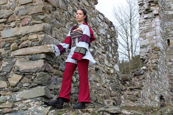 Woman models a Karen Heath design jacket and red trousers beside the wall of a castle