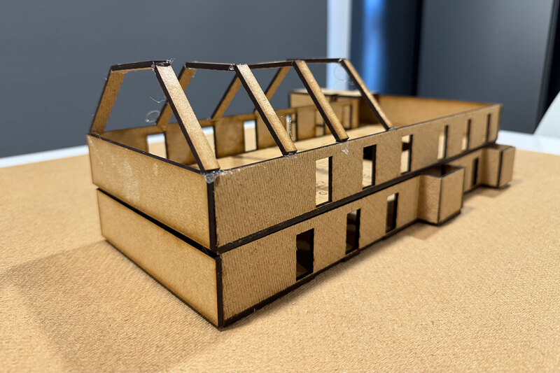 A cardboard model of a house with a roof, showcasing a miniature version of a residential structure.