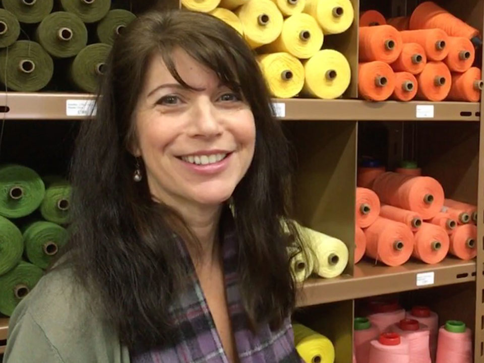 Marnie Collins standing before a shelf of green, yellow and orange yarn spools