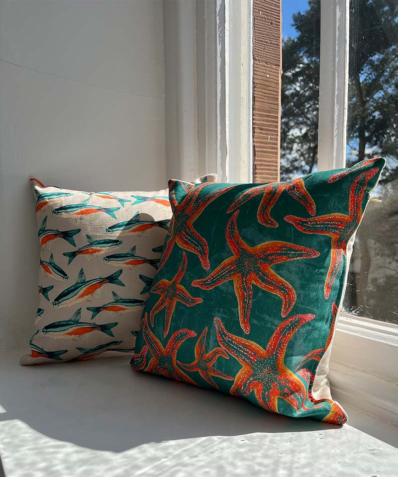 Two fish-designed pillows, one with a blue fish and the other with a starfish pattern, resting on a window seat..
