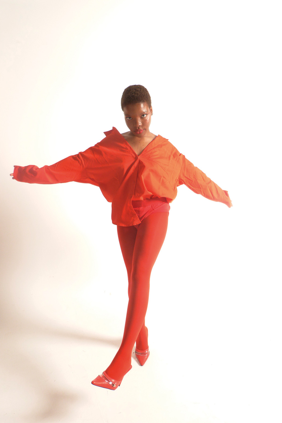 Woman in orange long sleeved blouse over orange tights and orange shoes swings a leg in front of her