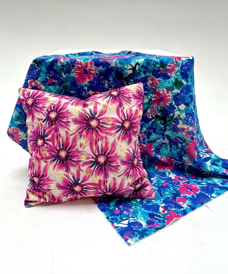 A floral pillow with pink patterns, sits on a blue and pink blanket..