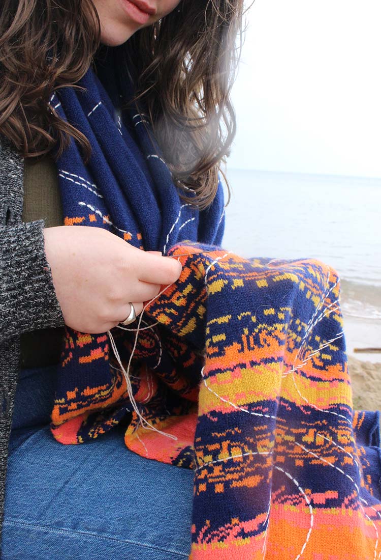 Woman sitting on the beach, admiring a blue and orange scarf.