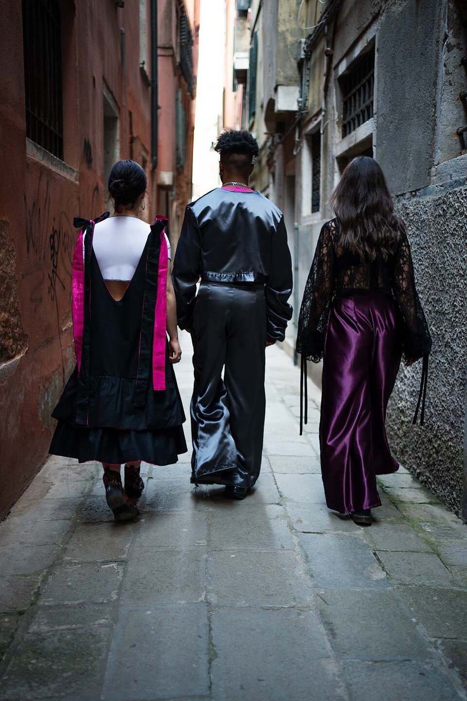 Rear view of a man and two women modelling Flamenco inspired streetwear from a collection by Paula Pacheco ina narrow street in Seville