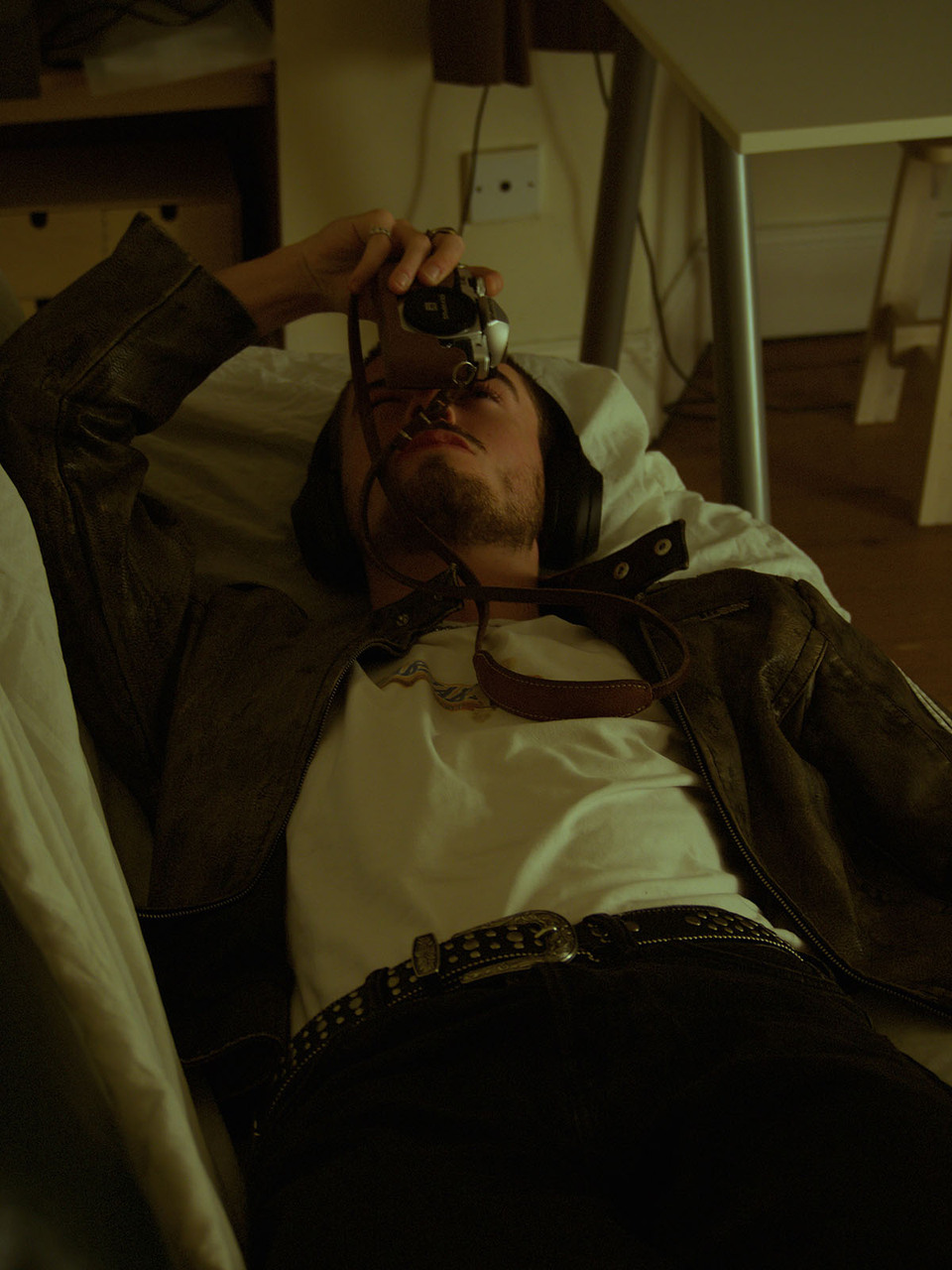 A man lies on a couch looking upwards through the viewfinder of a camera held in one hand