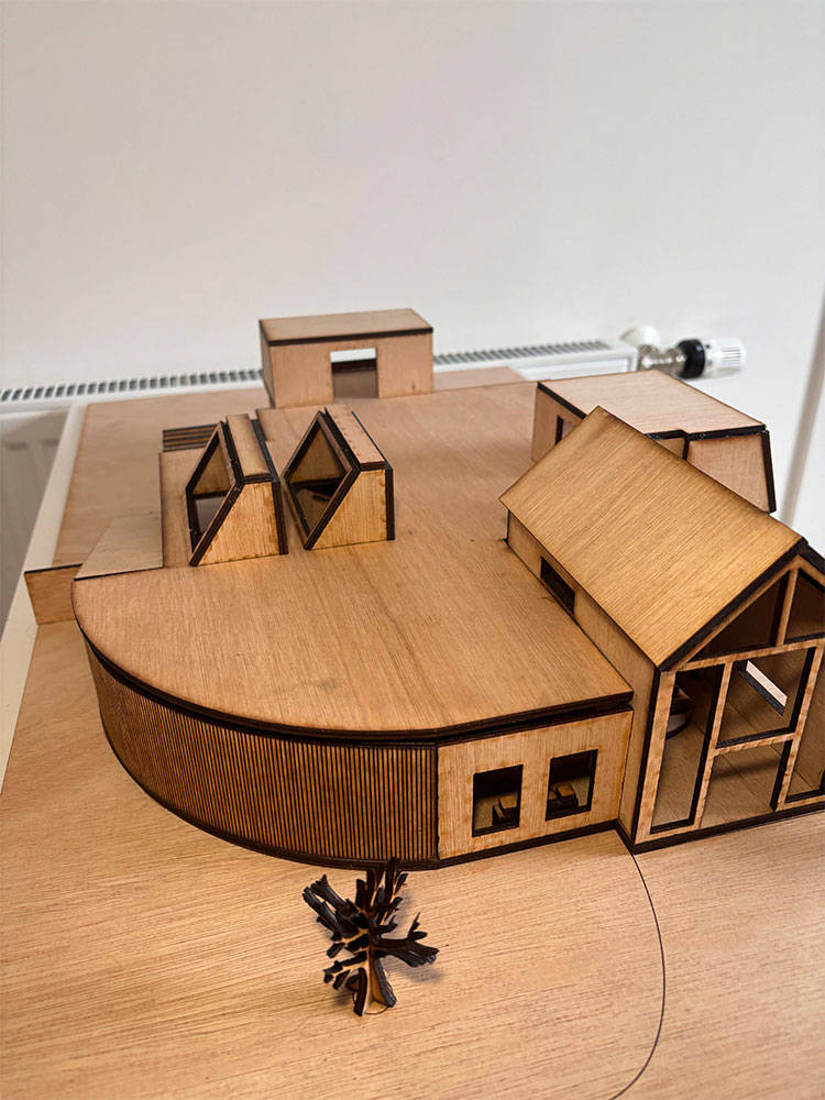 A scale model wooden house on a table with a tree.