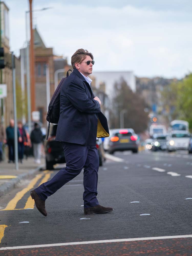 A man in a suit and sunglasses confidently crossing the street.
