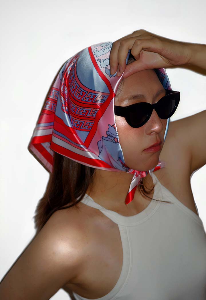 A stylish woman wearing sunglasses and a patterened silk headscarf.