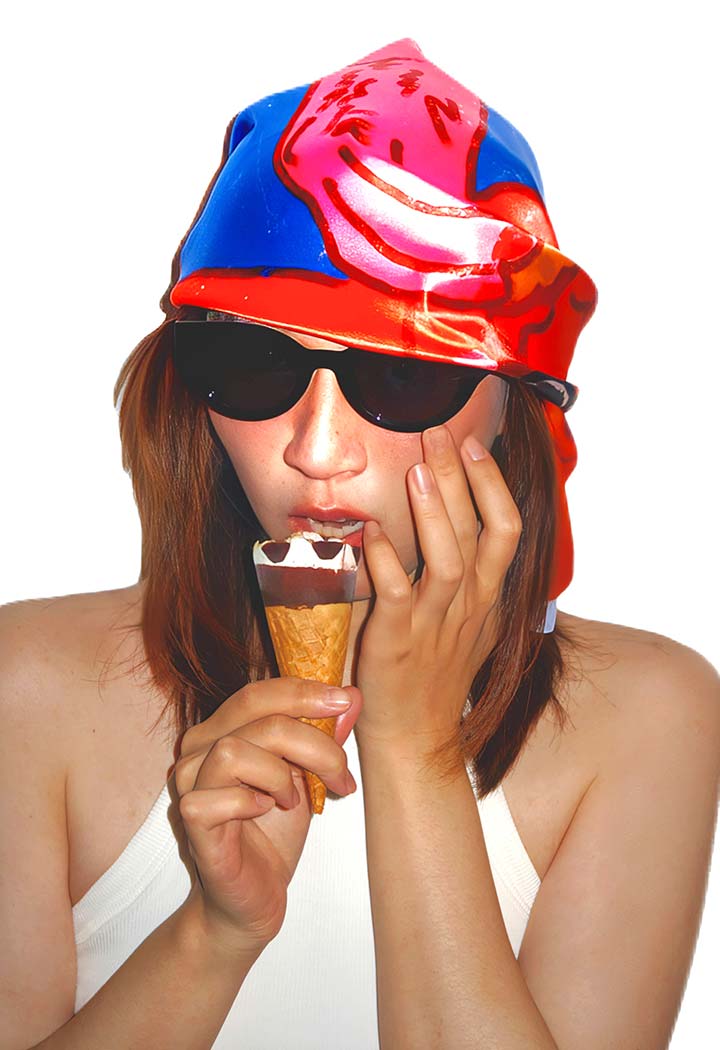 A woman wearing a colourful silk headscarf and sunglasses eating an ice cream cone.