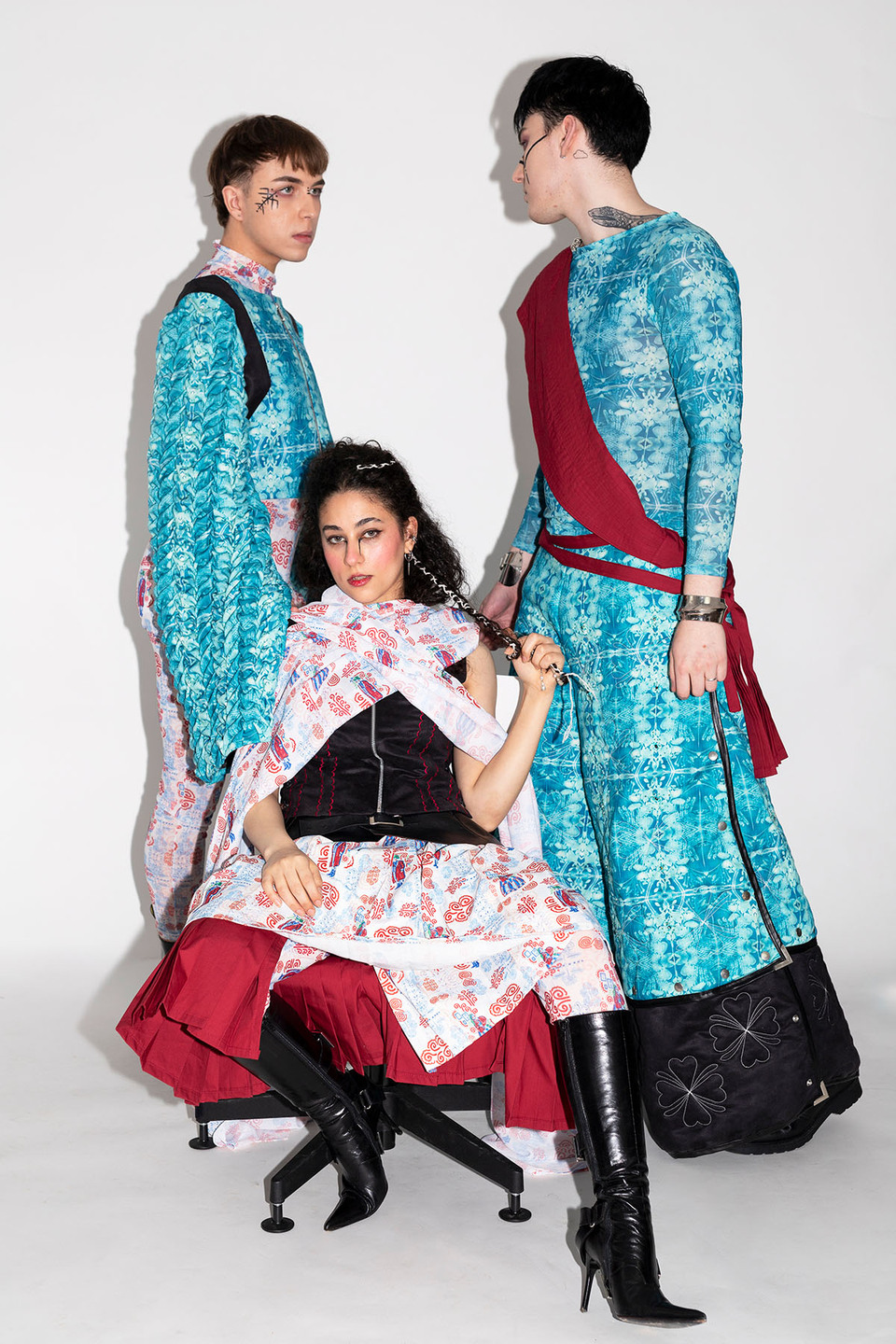 Woman seated wearing Slavic and Indian inspired skirt and scarves flanked by two young men in light blue tunic 