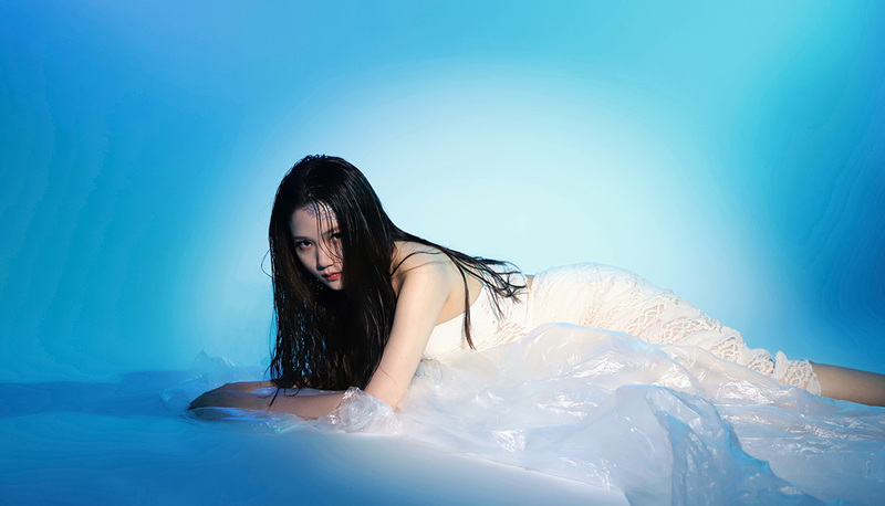 Young woman lies on a sheet of rumpled plastic against a white background giving the appearance of being in water
