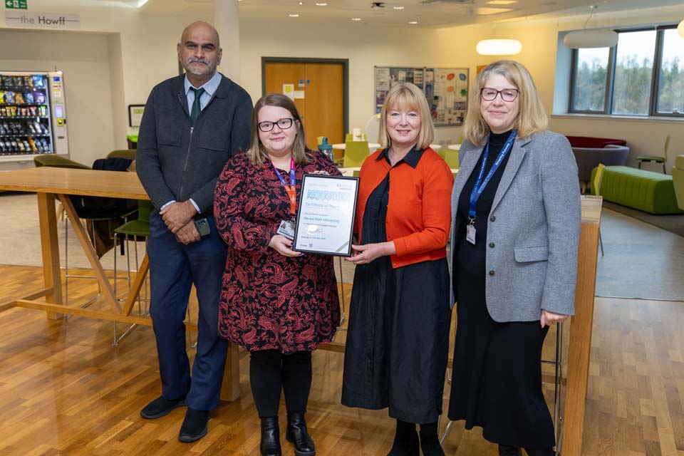 Four individuals proudly display a certificate while standing together.